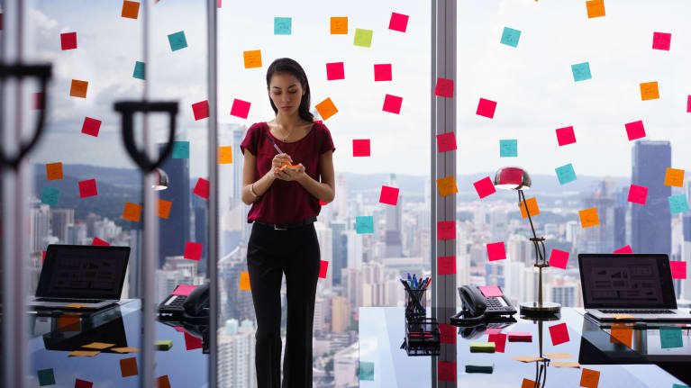 A woman standing in front of a desk with sticky notes on it.