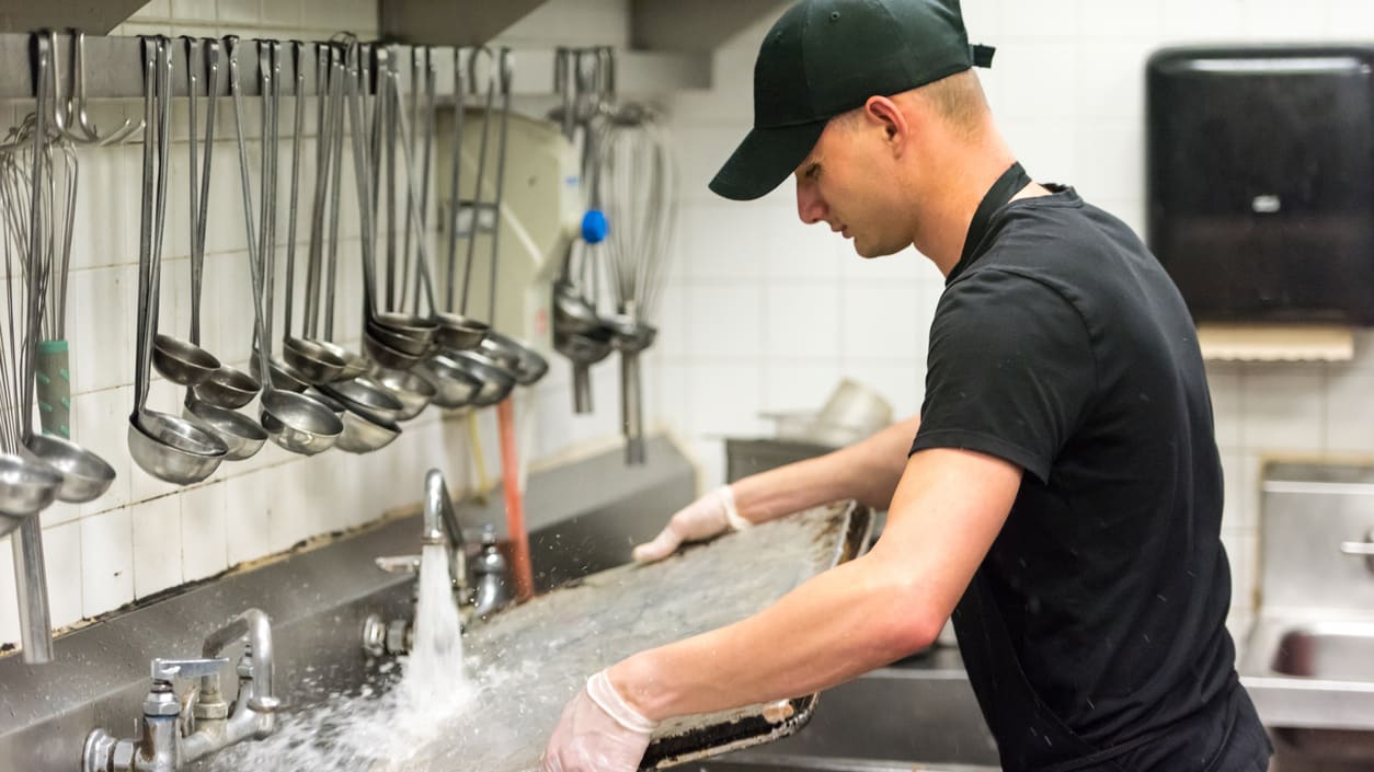 A man is washing dishes in a restaurant kitchen.