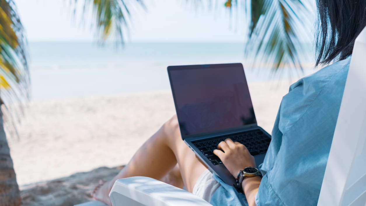 A woman sitting on a beach chair with a laptop.