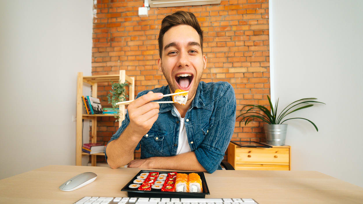 A man is eating sushi in front of a computer.