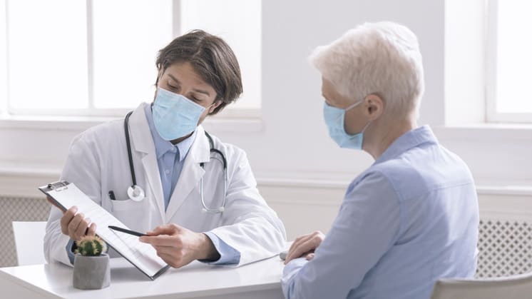 A man wearing a surgical mask is talking to an older woman.