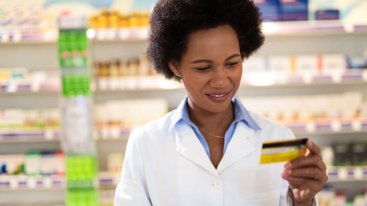 A woman in a lab coat holding a credit card in a pharmacy.