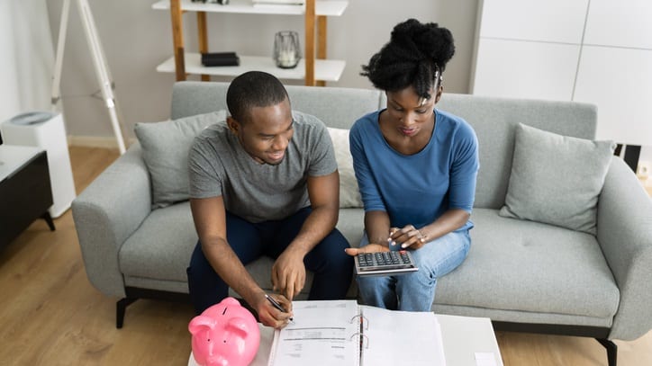 A man and woman sitting on a couch looking at a calculator.