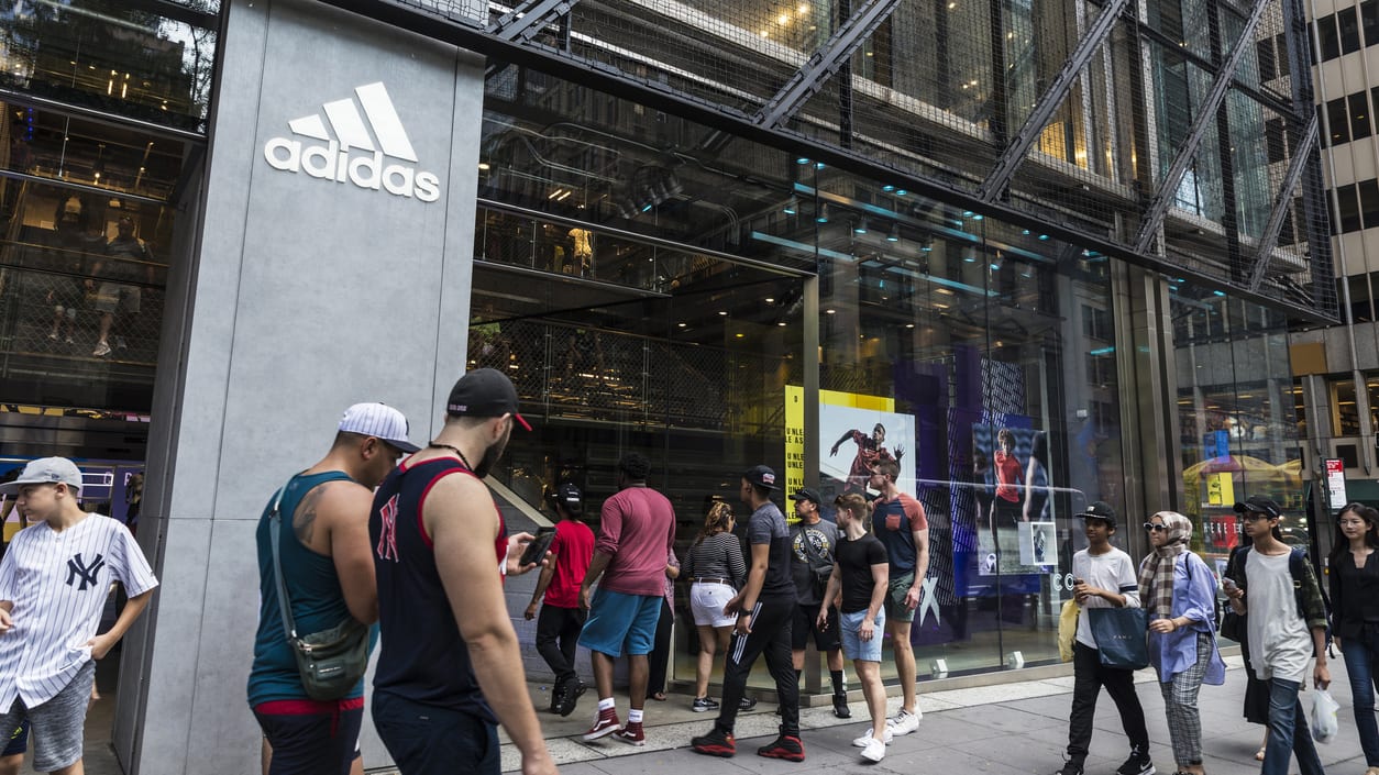 A group of people standing outside of an adidas store.