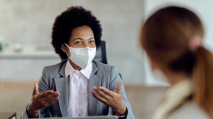 A woman wearing a face mask is talking to another woman in an office.