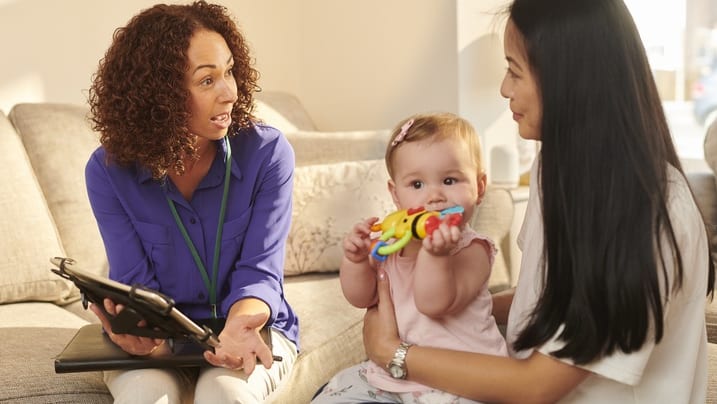 A woman is talking to a baby on a couch.