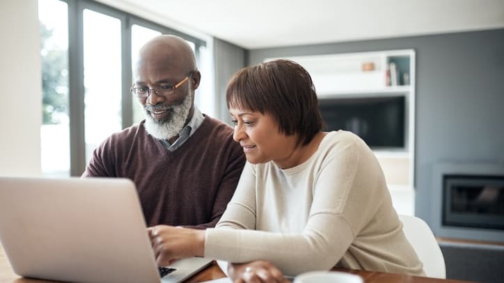 A man and woman looking at a laptop while sitting at a table.