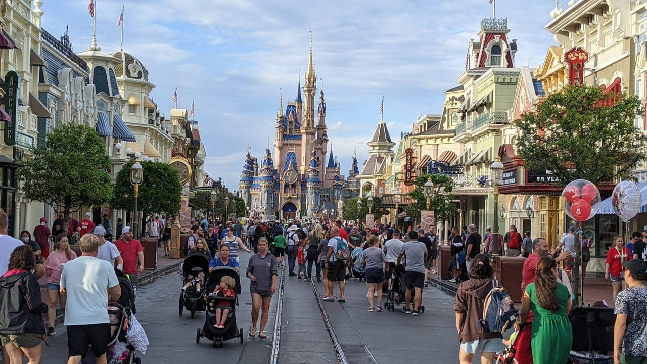 A crowded street in disney world with cinderella castle in the background.