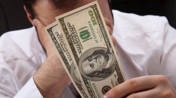 A man covering his face with a dollar bill.