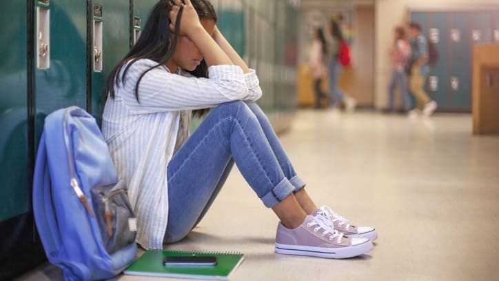 A girl sitting on the floor in a school hallway.