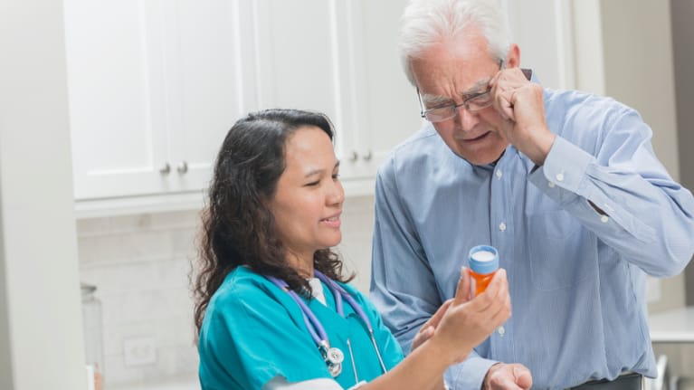 A nurse is looking at a pill bottle with an older man.
