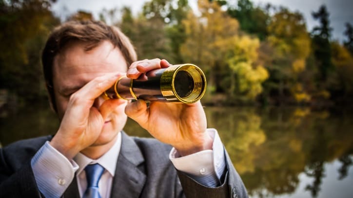 A man in a suit looking through binoculars.