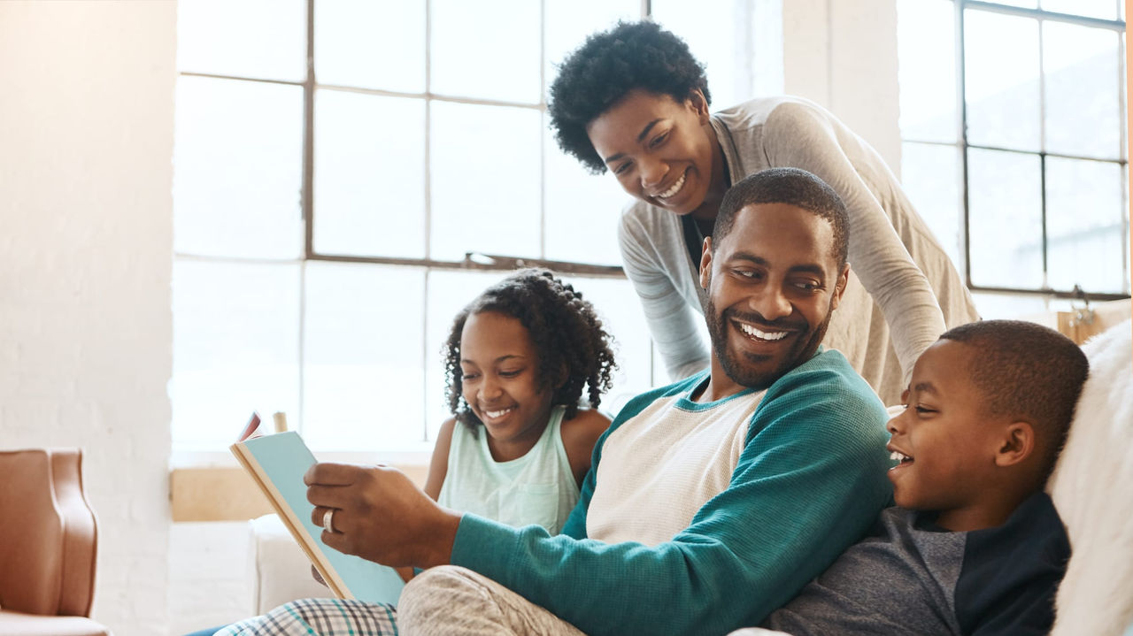 A family sitting on a couch reading a book.