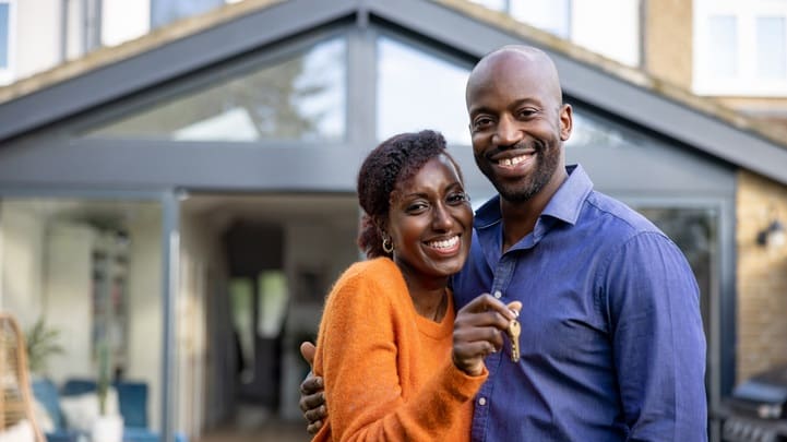 A couple holding a house key in front of their new home.