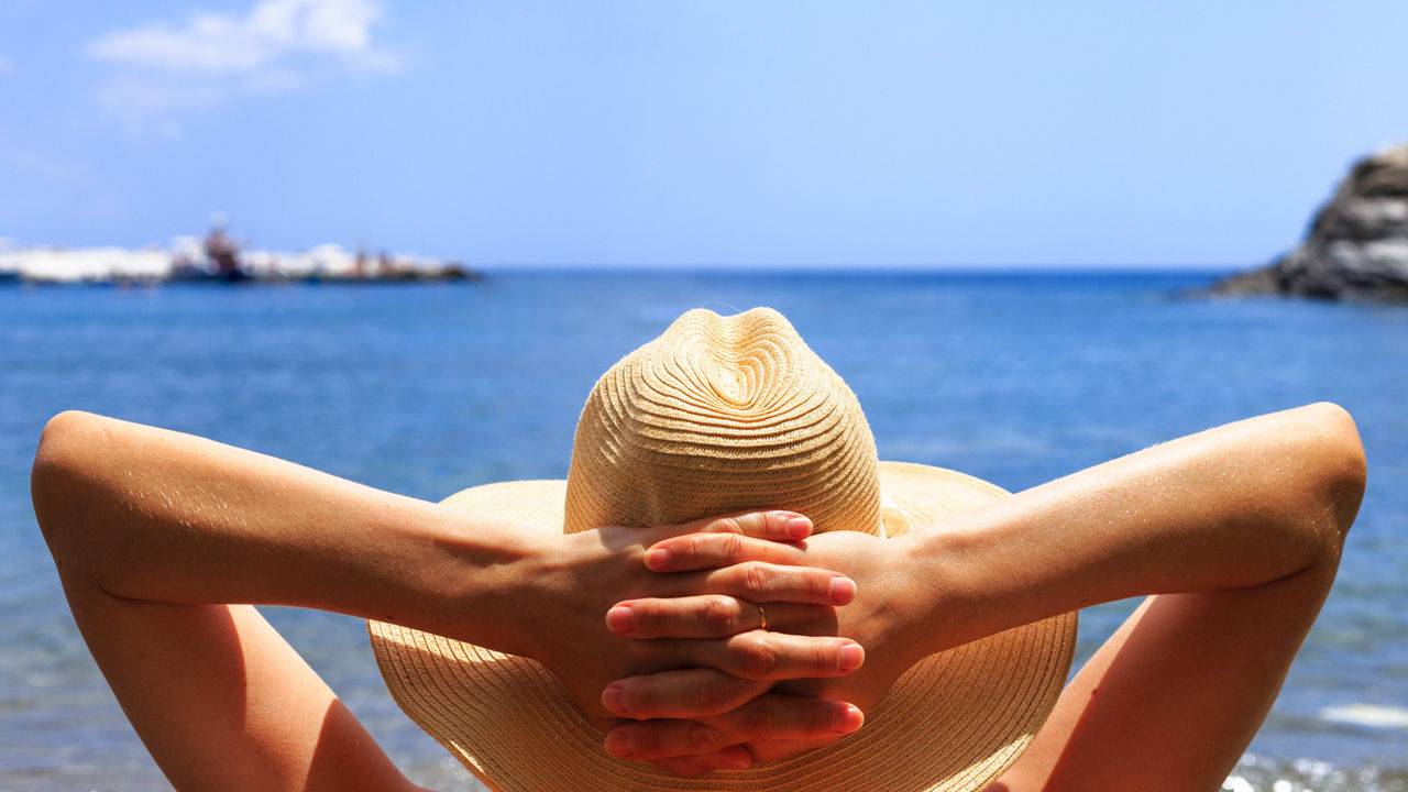 A woman in a hat is relaxing on the beach.