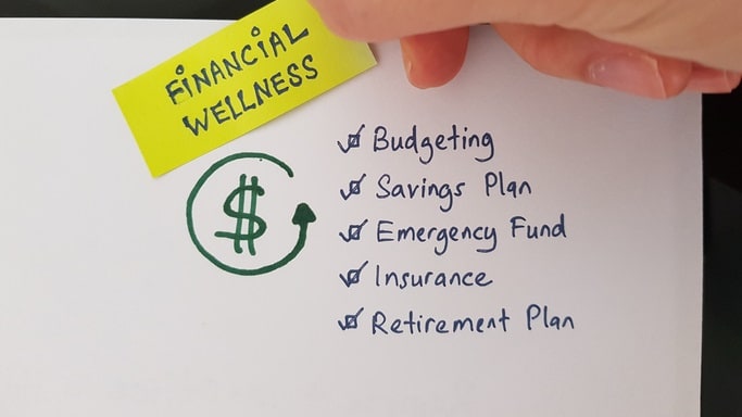 A person is putting a sticky note on a piece of paper that says financial wellness.