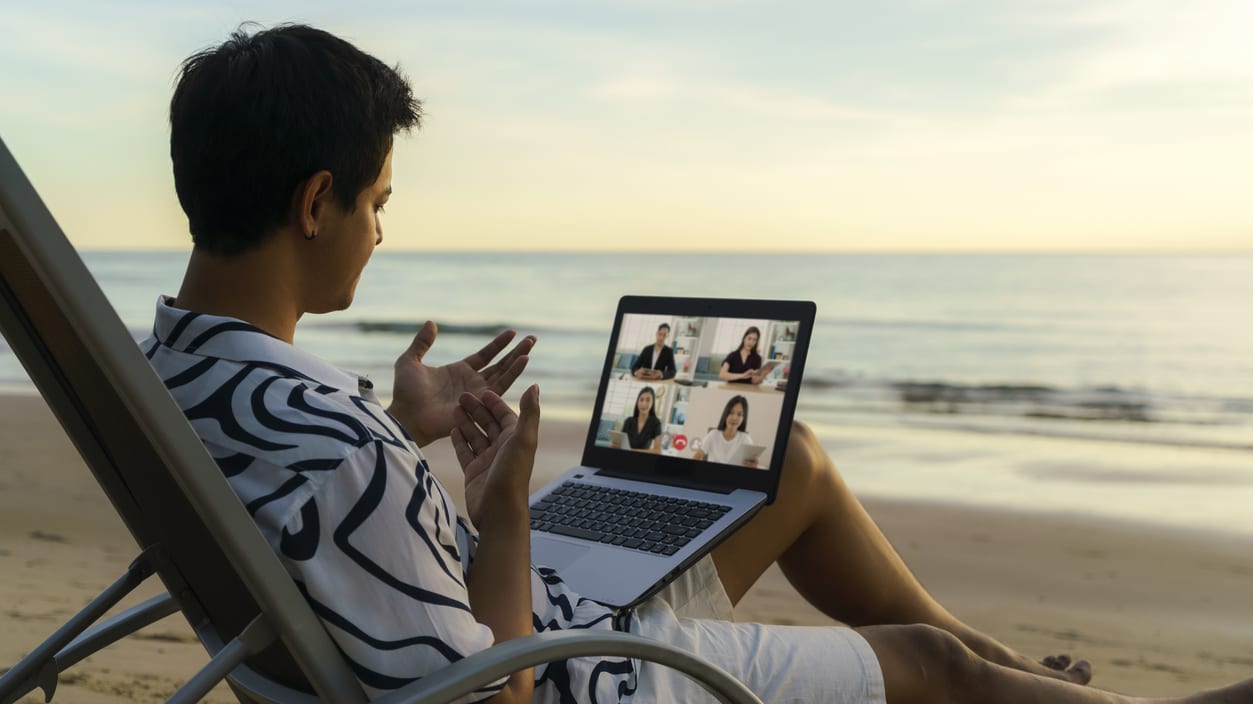 A man sitting on a beach chair with a laptop on his lap.