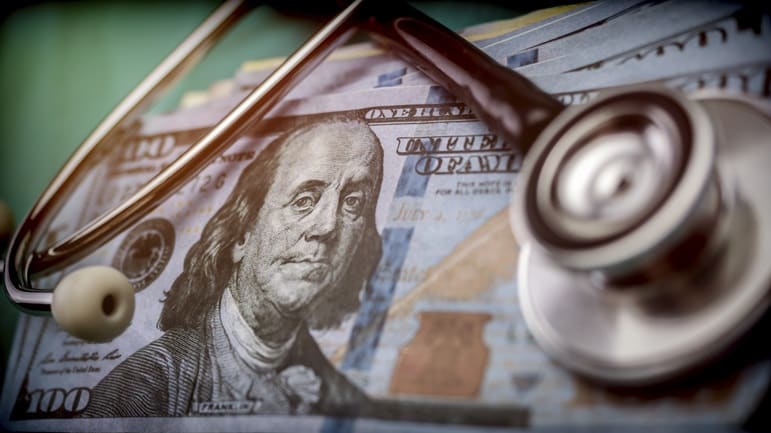 A stethoscope sits on top of a stack of money.