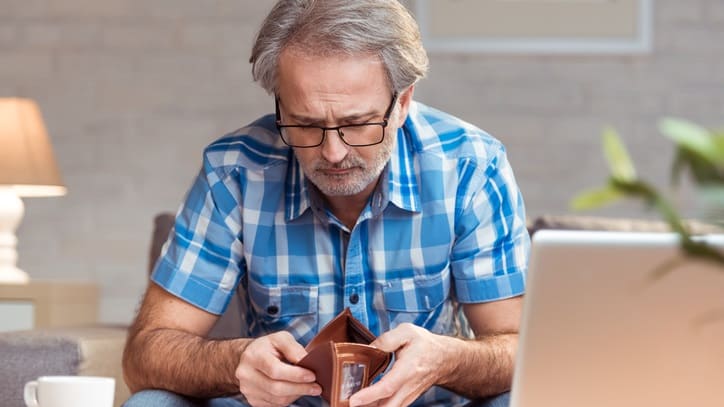 A man is looking at his wallet while sitting on a laptop.