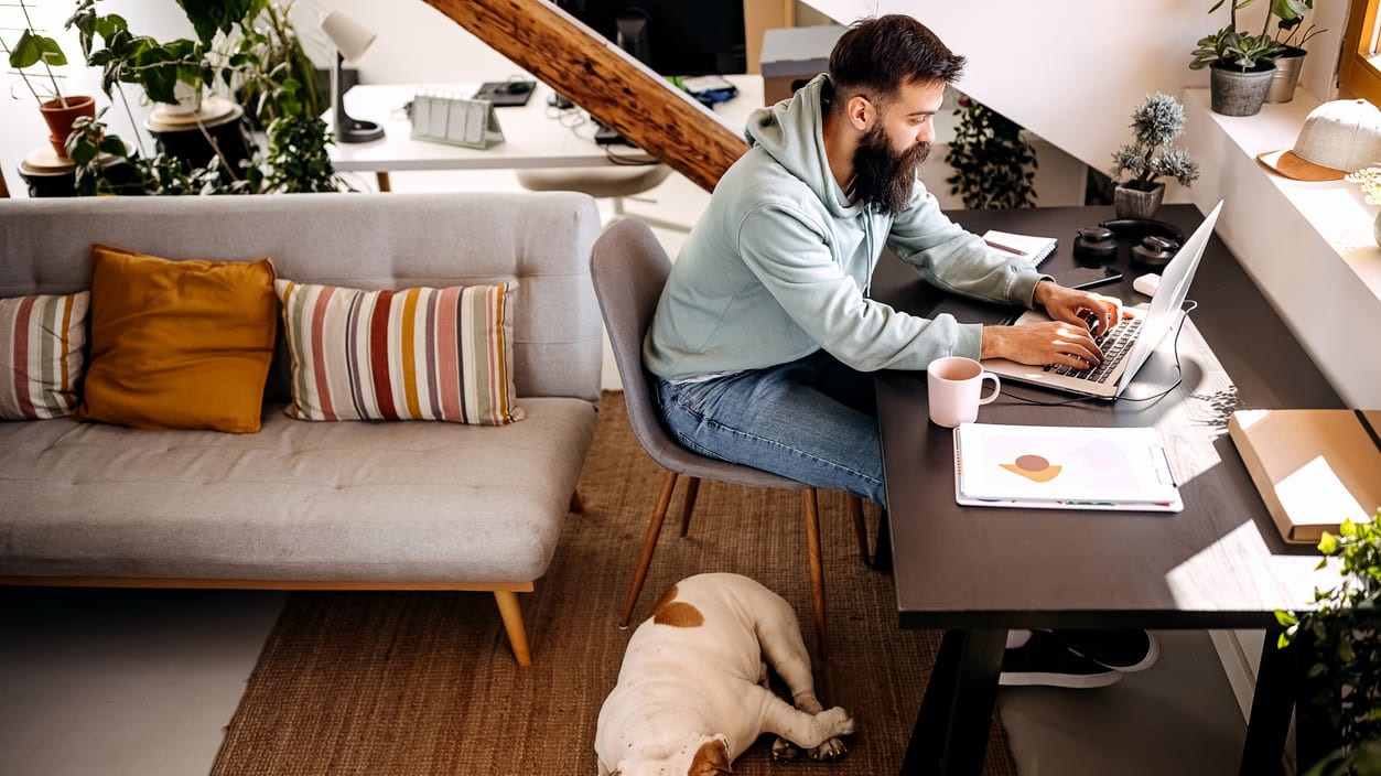 A man working on his laptop at home with his dog.