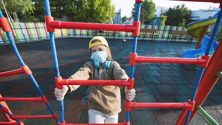 A boy wearing a face mask in a playground.