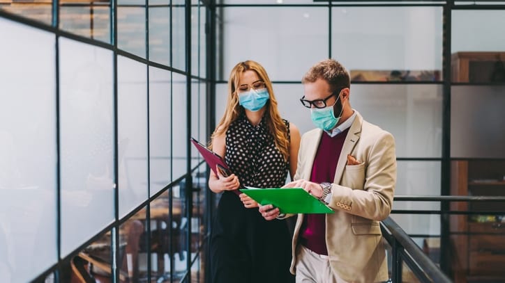 Two people wearing surgical masks in an office.
