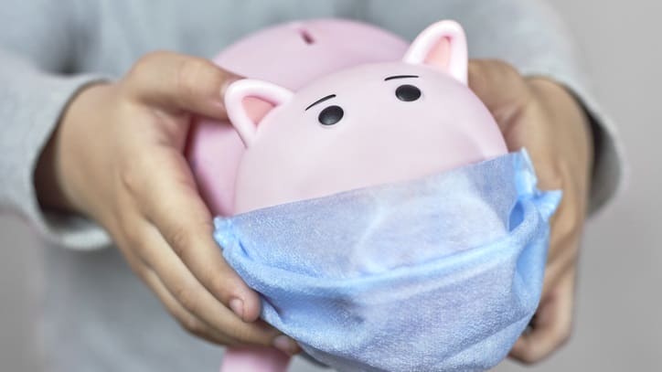 A child holding a pink piggy bank with a medical mask on it.