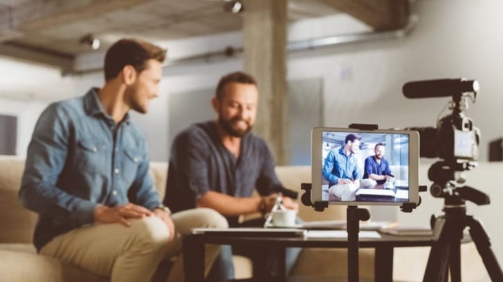 Three men sitting on a couch with a video camera.