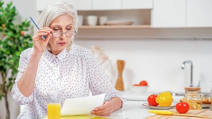 An older woman is sitting at the kitchen counter looking at a piece of paper.