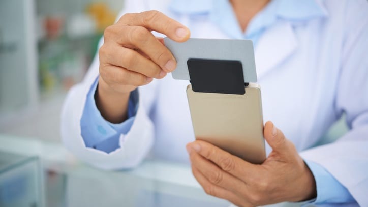 A doctor holding up a credit card in a pharmacy.