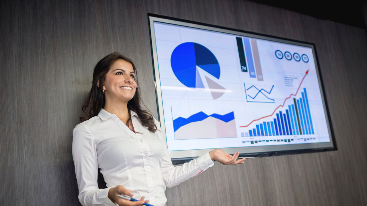 A business woman is standing in front of a board with graphs on it.