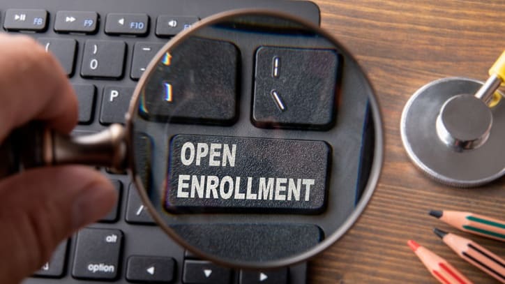 A person holding a magnifying glass over the word open enrollment.
