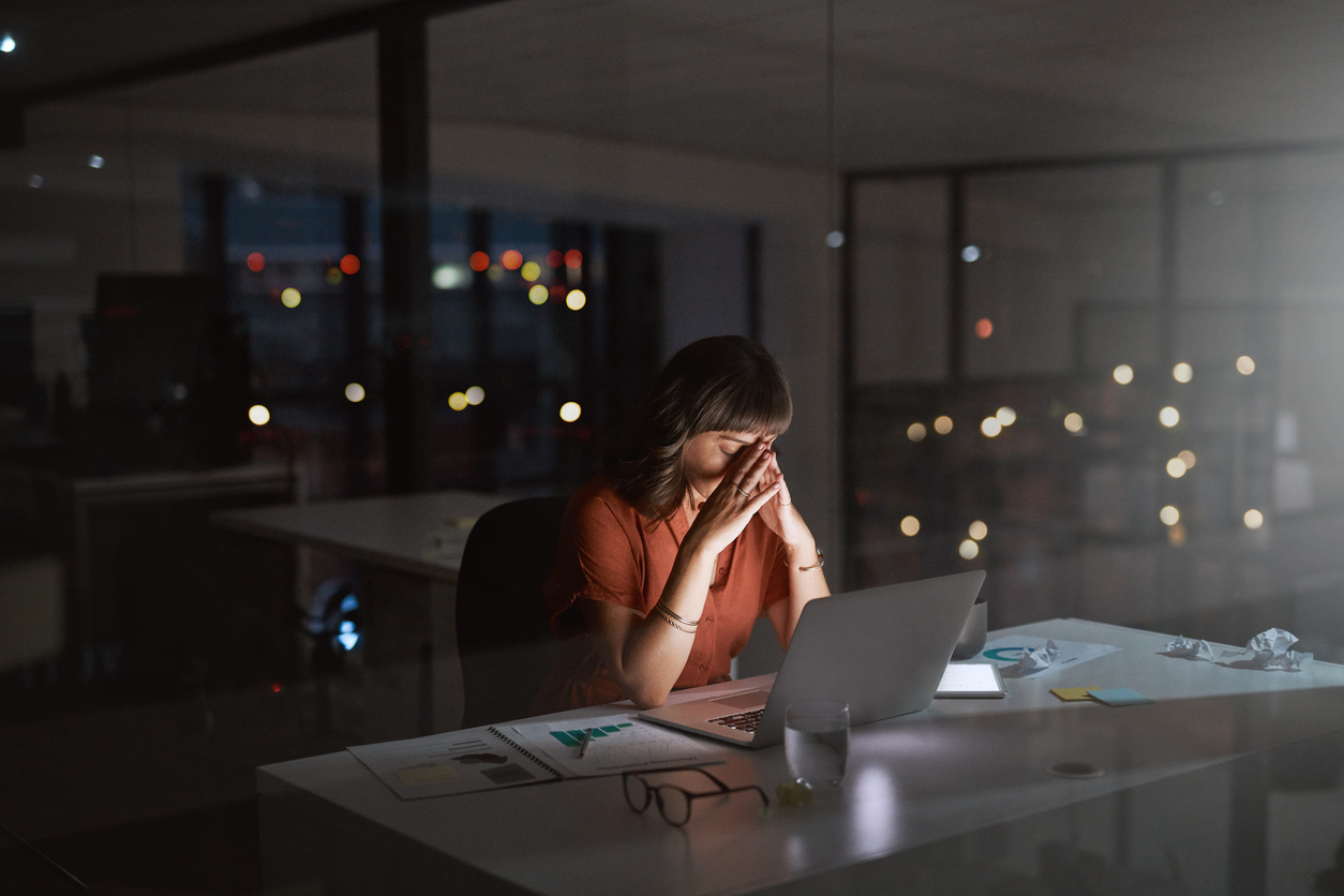 Person at their desk at night with their hands on their head, signaling burnout