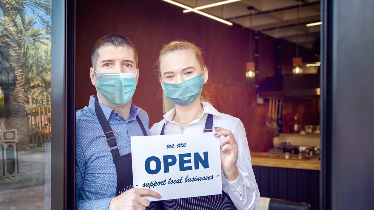 A couple wearing surgical masks holding a sign that says open.