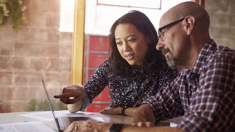 Two people sitting at a table looking at a laptop.