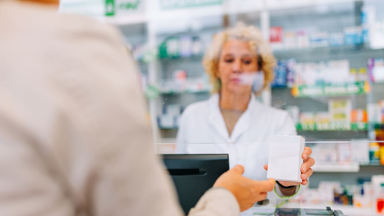 A pharmacist is handing a prescription to a customer in a pharmacy.