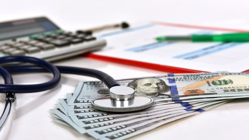 A stethoscope sits on top of money and a calculator.