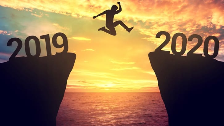 A man jumps over a cliff with the year 2020 written on it.