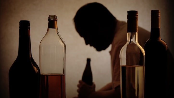 A man is silhouetted in front of several bottles of alcohol.