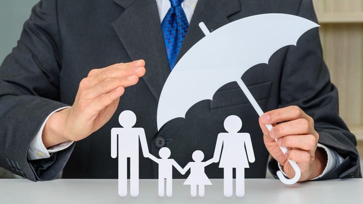 A man in a suit holding a paper umbrella over his family.