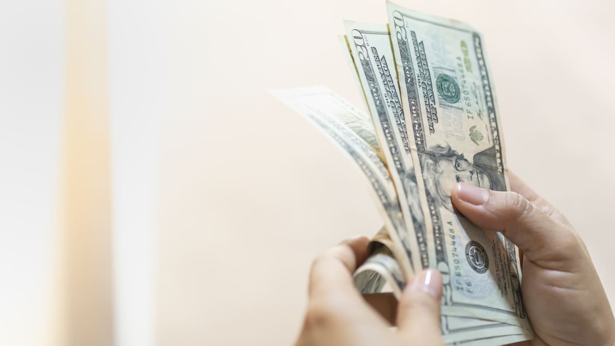 A woman's hand holding a stack of dollar bills.