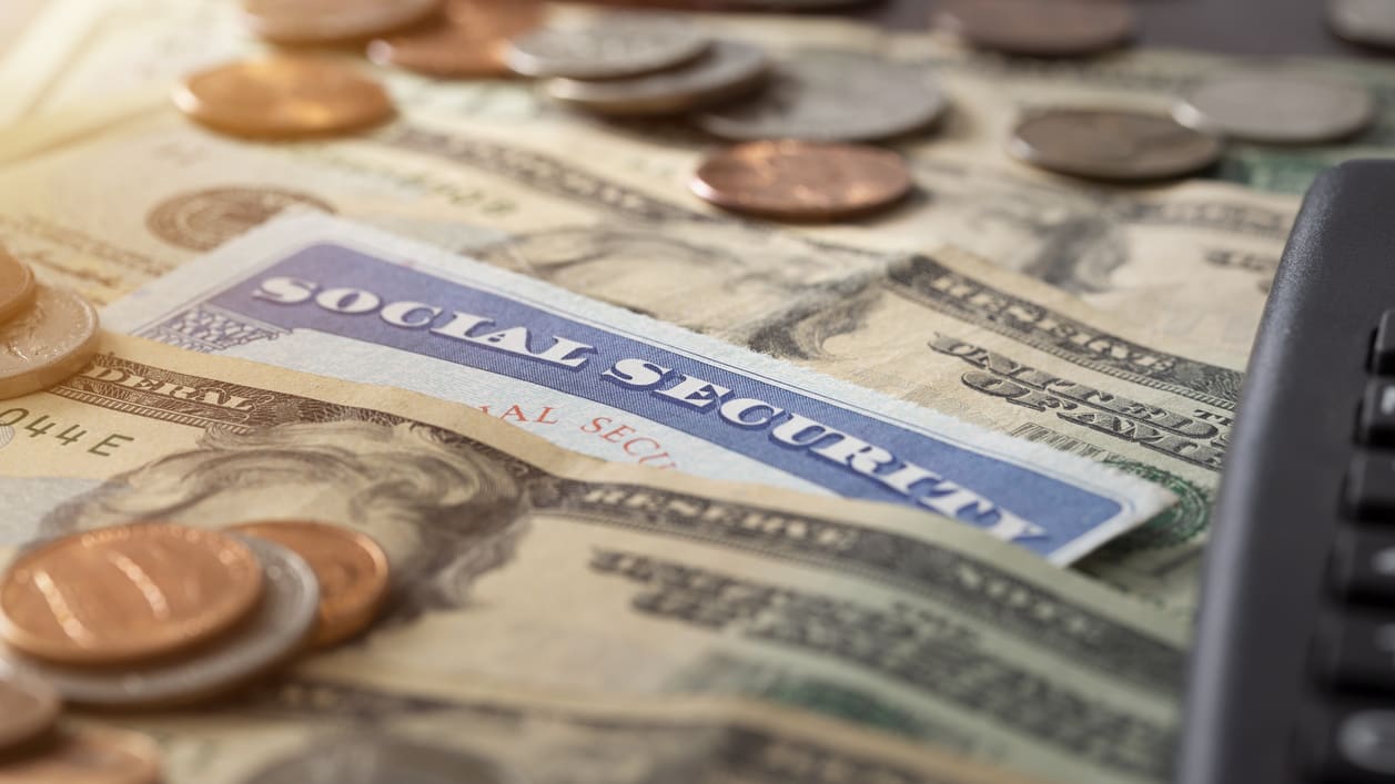 A social security card on top of a pile of money and a calculator.