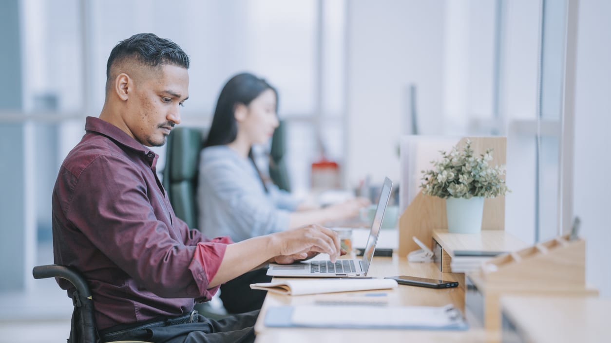 A man in a wheelchair using a laptop in an office.