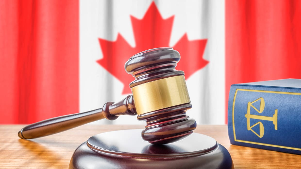 A judge's gavel and a book on a table with a canadian flag in the background.