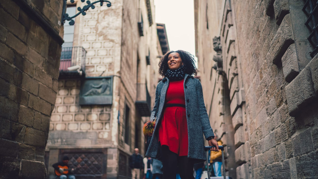 A woman walking down an alley with a suitcase.