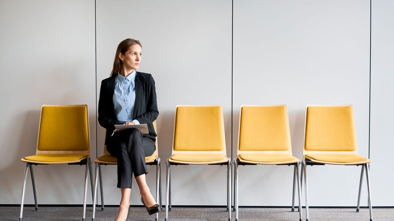 A business woman sitting in a row of yellow chairs.