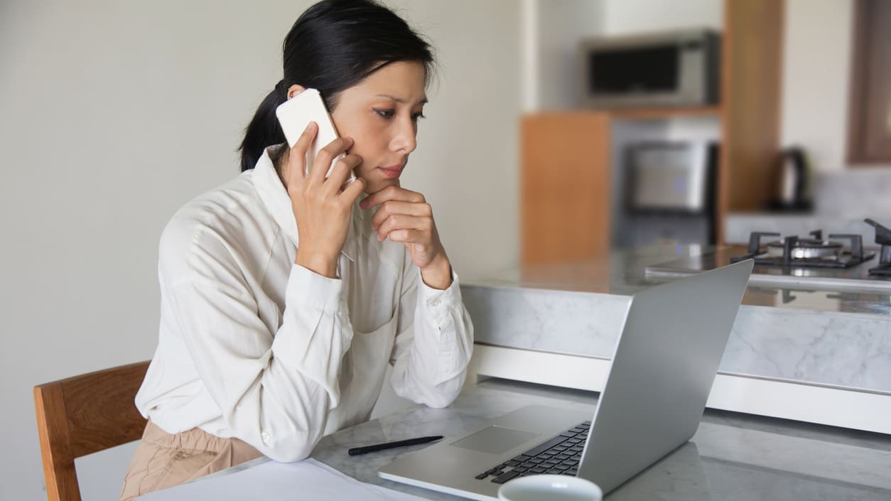 A woman talking on the phone while sitting at a table with a laptop.