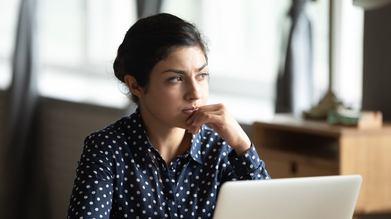 A woman sitting at a table looking at her laptop.