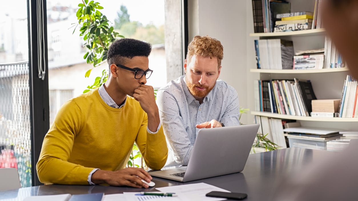 Two men sitting at a table looking at a laptop.