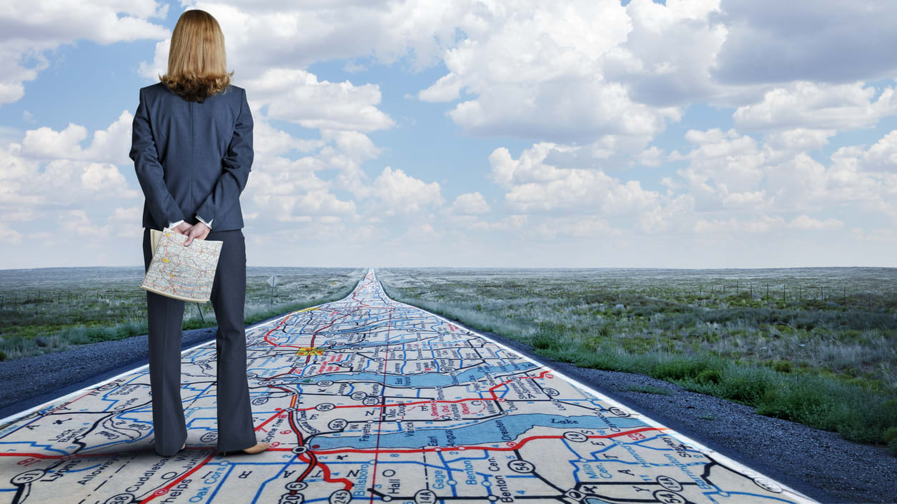 A business woman standing on a road with a map.